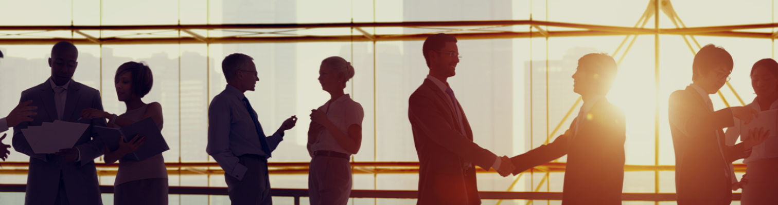Silhouettes of business people shaking hands in front of a modern building, symbolizing partnership and collaboration.