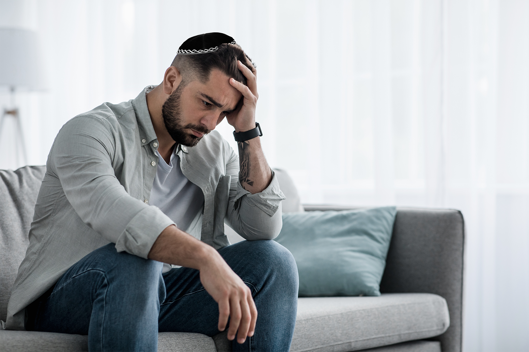 Young man sits on couch with head in hand.