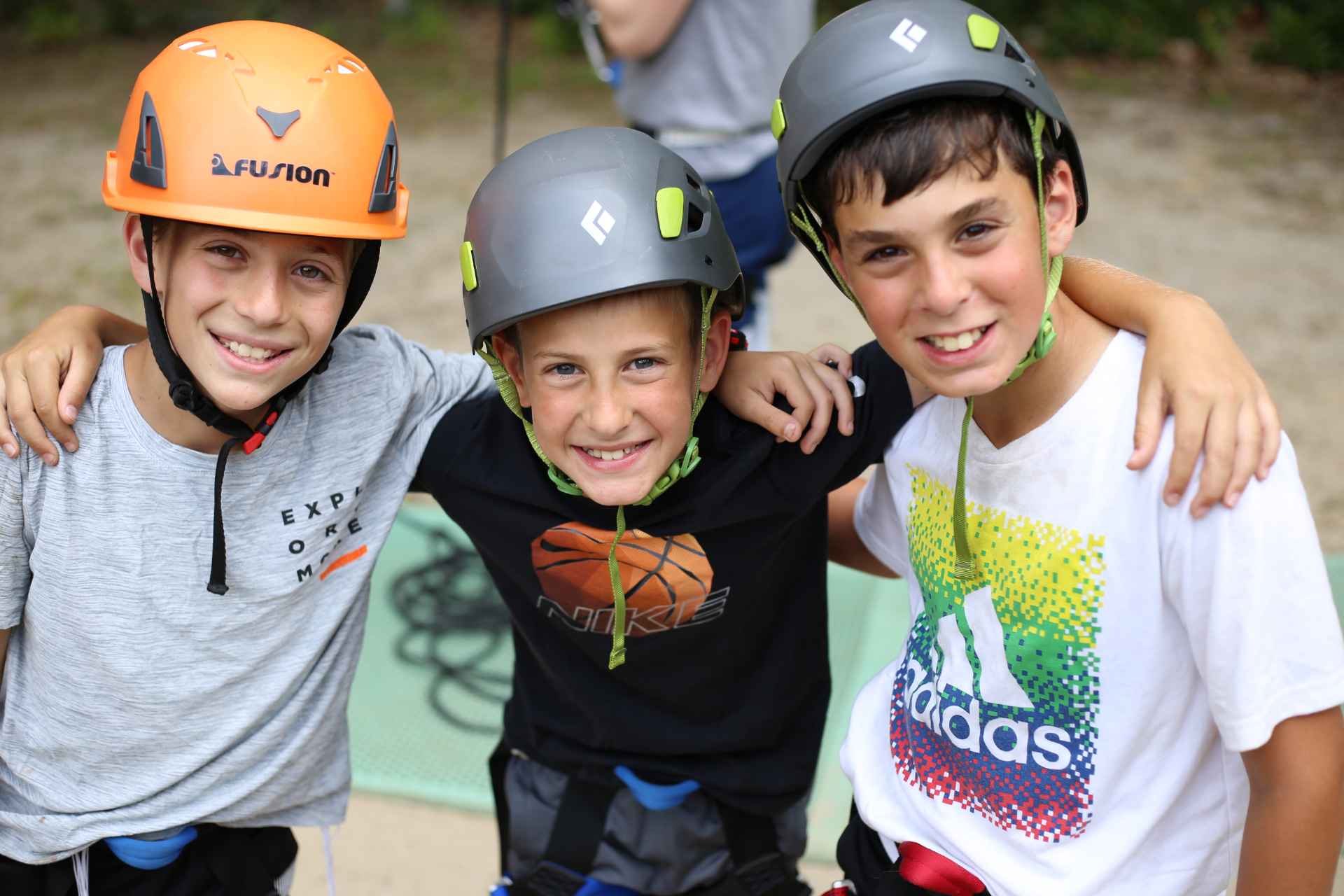 3 Camp aged children in climbing smile with their arms around each other.