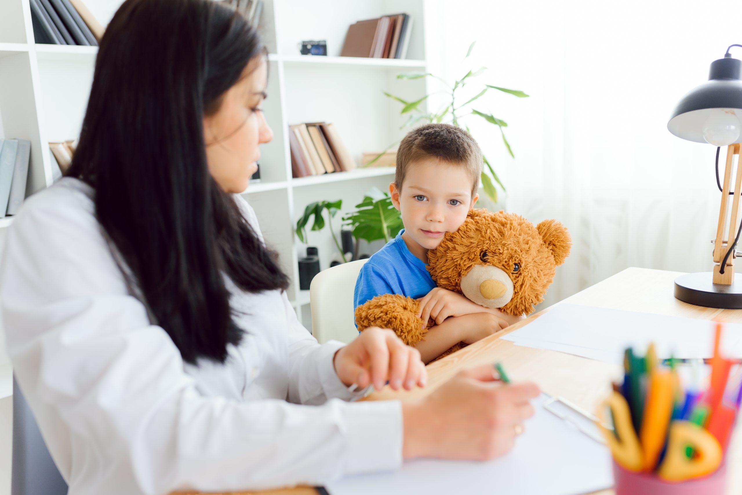 Young boy holding teddy bear in therapy with a female therapist.