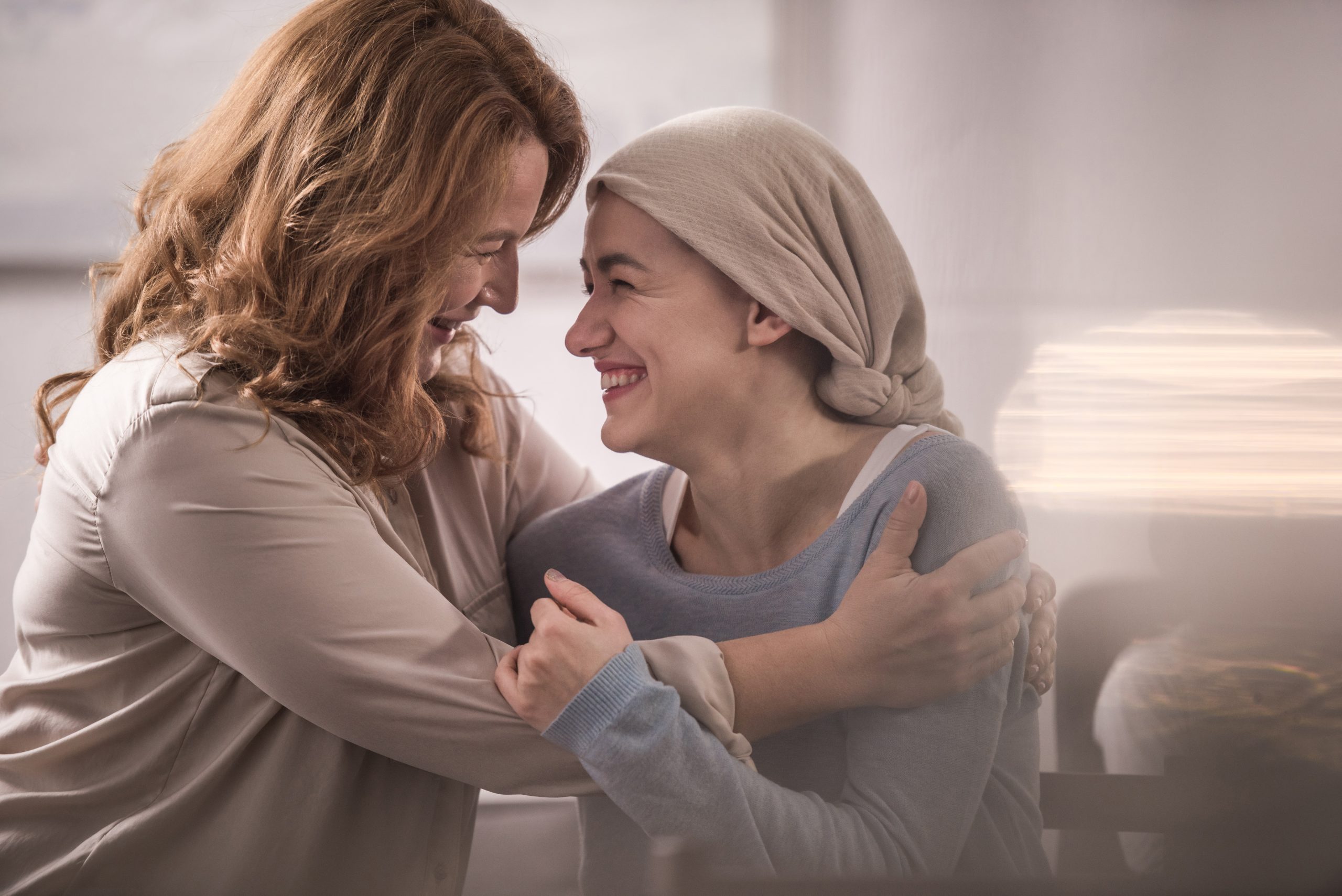 Happy mother and adult daughter in tichel hugging and looking at each other.