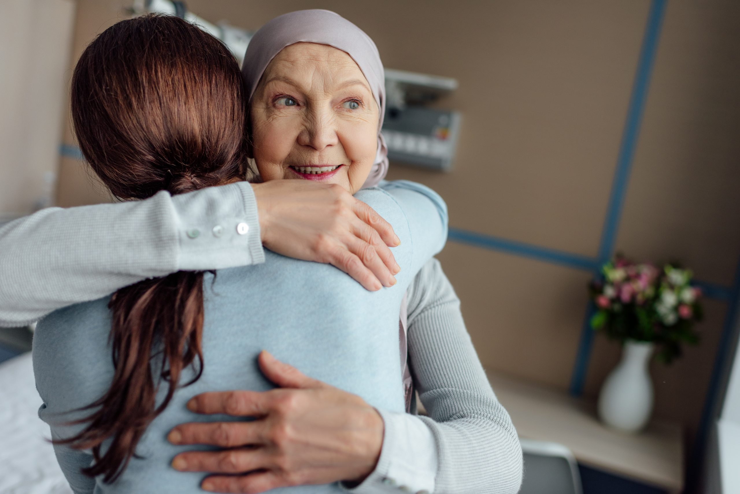 smiling senior woman in kerchief hugging daughter in hospital