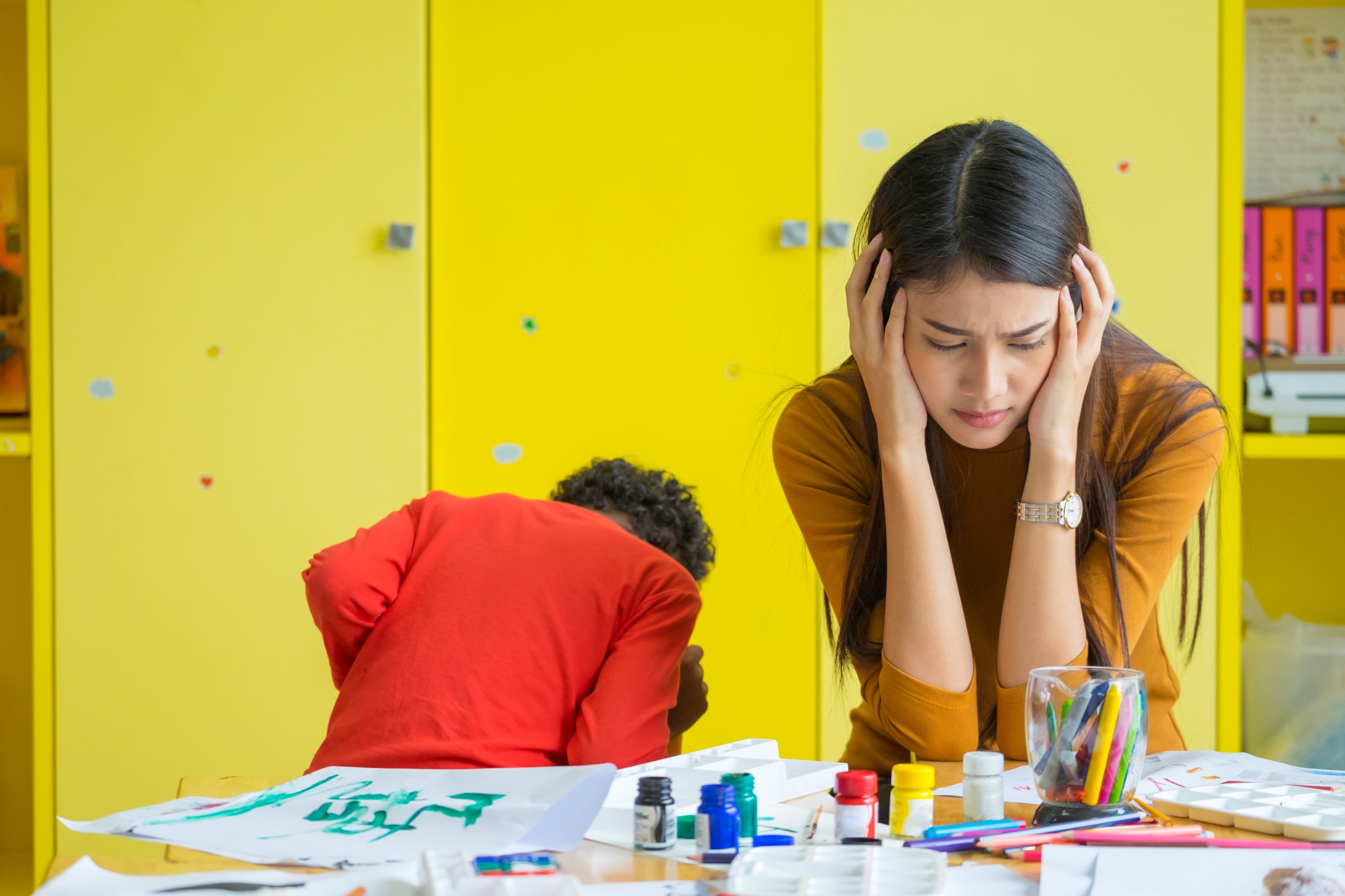 Frustrated Teacher sites with student in background.