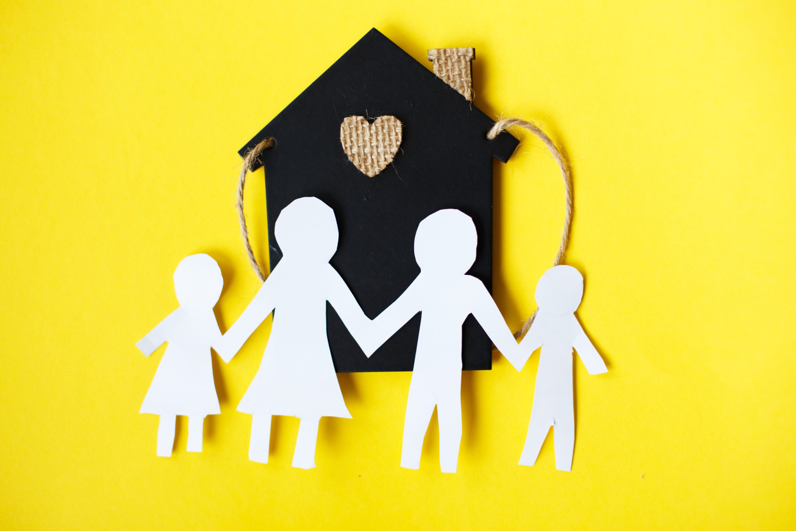 Happy paper cut family holding hands on yellow background near little toy house.