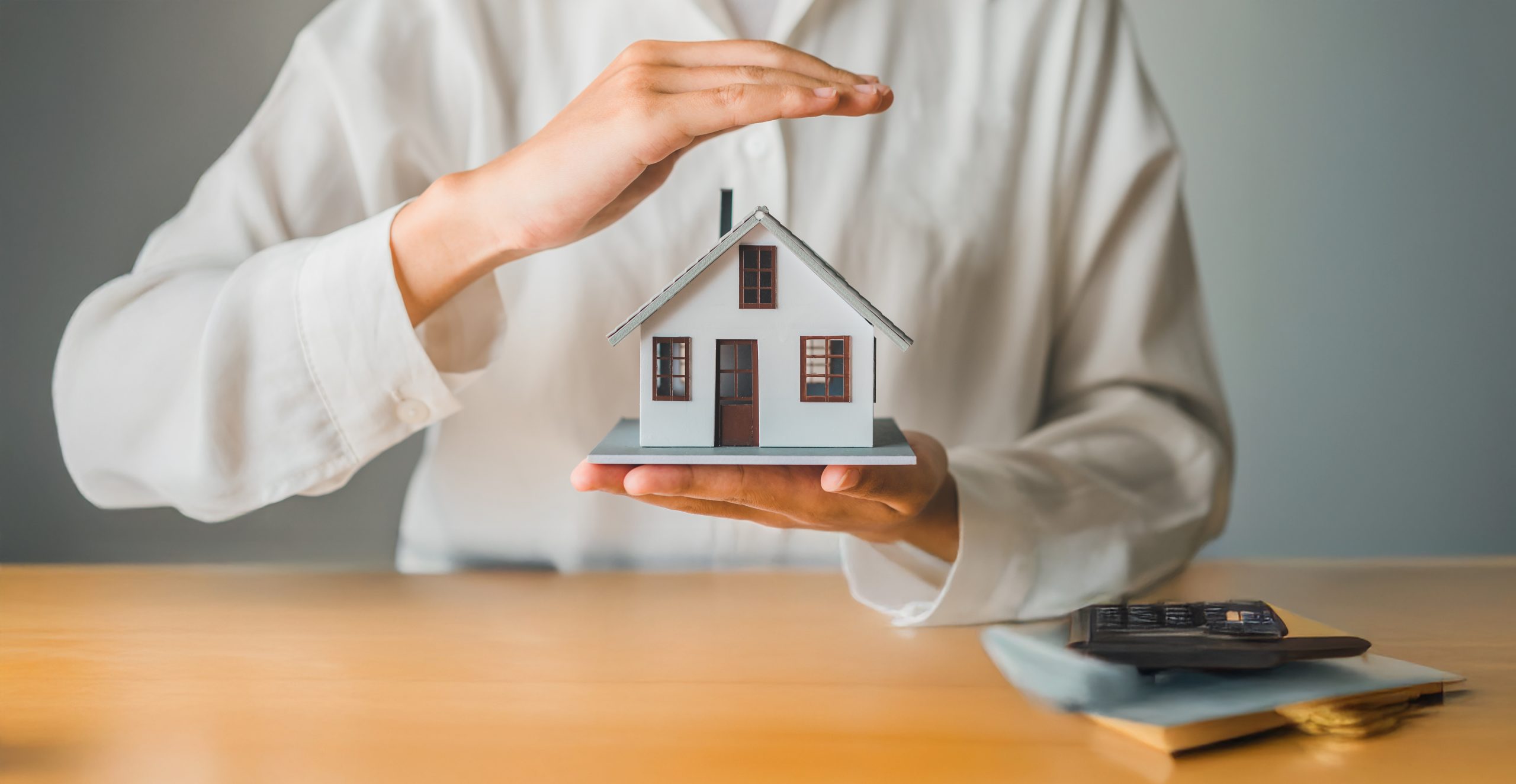 Hand holding small house from the bottom with other hand sheilding the house from the top.