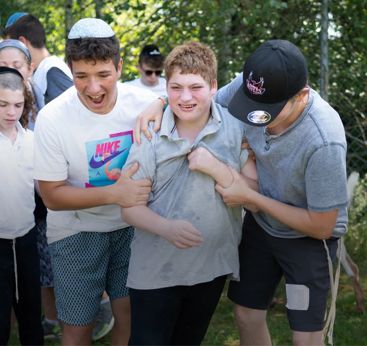 A group of children engage in playful tugging during an outdoor activity, surrounded by greenery and a chain-link fence.