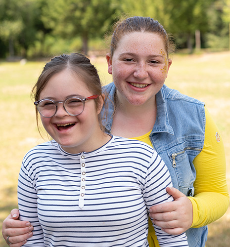 Two young woman smile and embrace in a camp bunk.