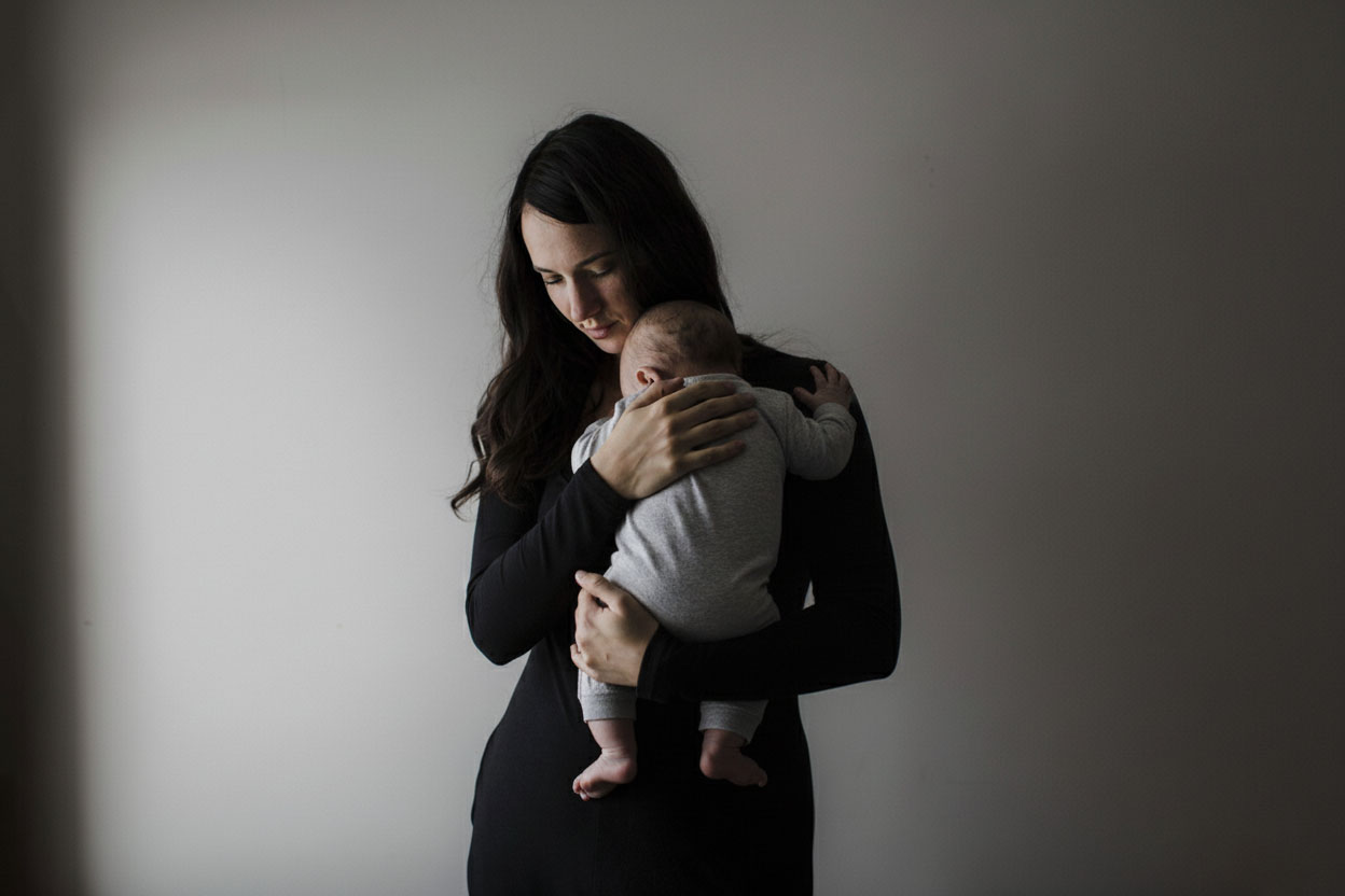 Woman holds baby in low light with sad expression